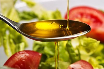 Vegetable Oil Pouring Into Metal Spoon Over Green Salad
