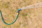 Hose Spraying Water On Dried Lawn