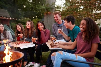 Teenagers In A Backyard Eating Food Around A Fire Pit