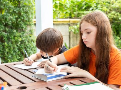 Two Children Writing On A Table In The Garden