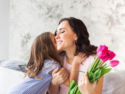Woman Holding Bouquet Of Flowers Hugging A Little Girl
