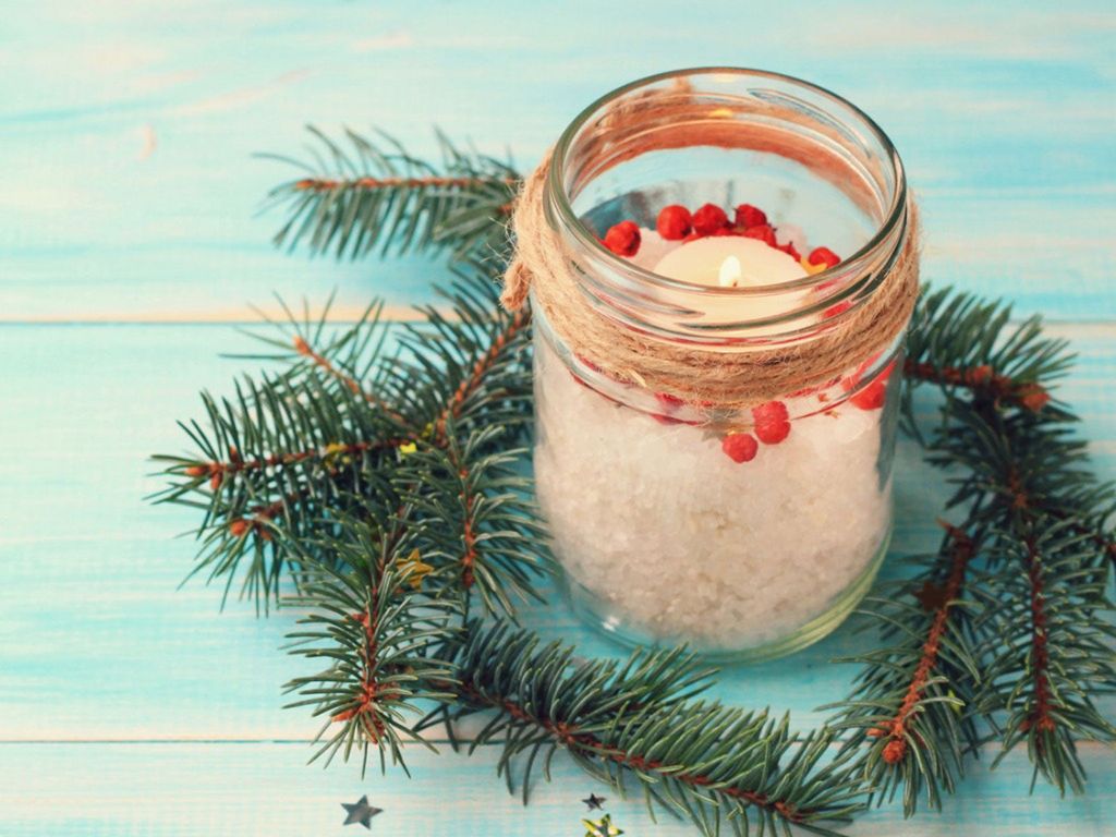 A candle in a jar encircled with evergreen twigs