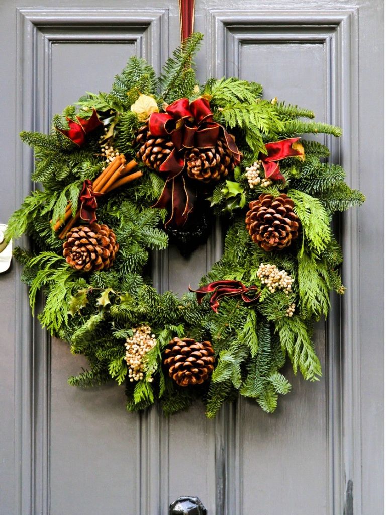 An evergreen wreath with pinecones hanging on a door