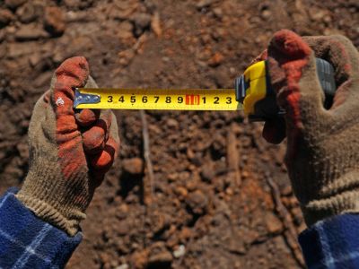 A gardener in work gloves holds a tape measure in centimeters