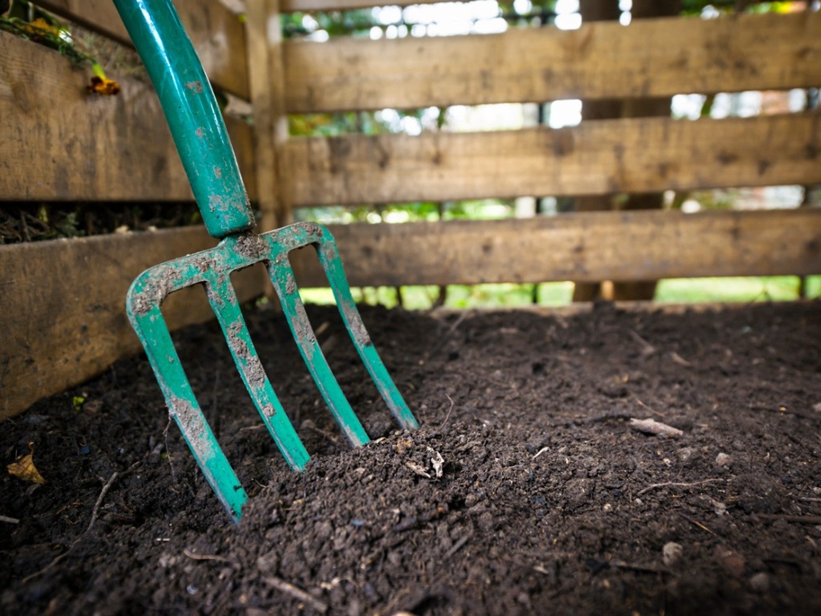 A teal pitchfork rests in a compost bin