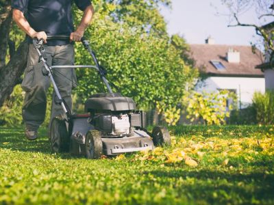 A man runs his lawnmower over fallen leaves on the lawn