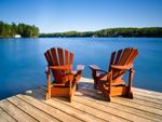 Two Adirondack chairs sit on a dock overlooking a lake