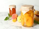 Jars of preserved peaches surrounded by whole and halved peaches