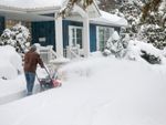 A man plows a driveway through deep snow with a snowblower