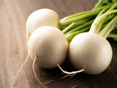 Three round white turnips with stems sit on a wooden surface
