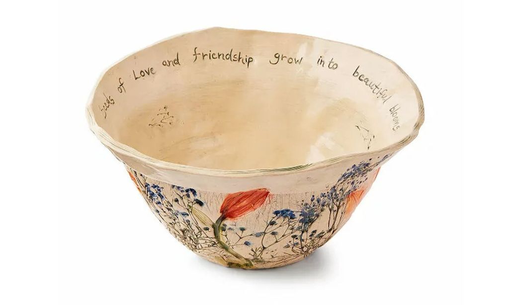 A serving bowl with handpainted flowers on the outside and "seeds of love and friendship grow into beautiful blooms" written on the inside.