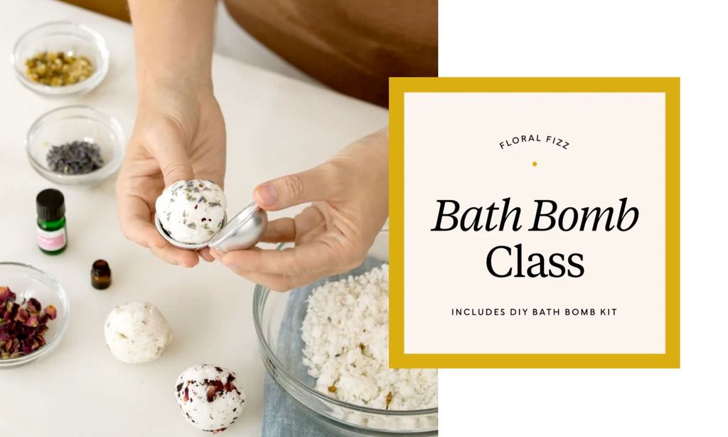 A person making a bath bomb, with essential oils, dried flowers, and other bath bombs on the table.
