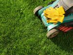 A lawnmower and yellow gloves on a lush green lawn