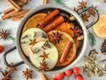 A metal pot of wassail with orange, apples, star anise, and cinnamon sticks
