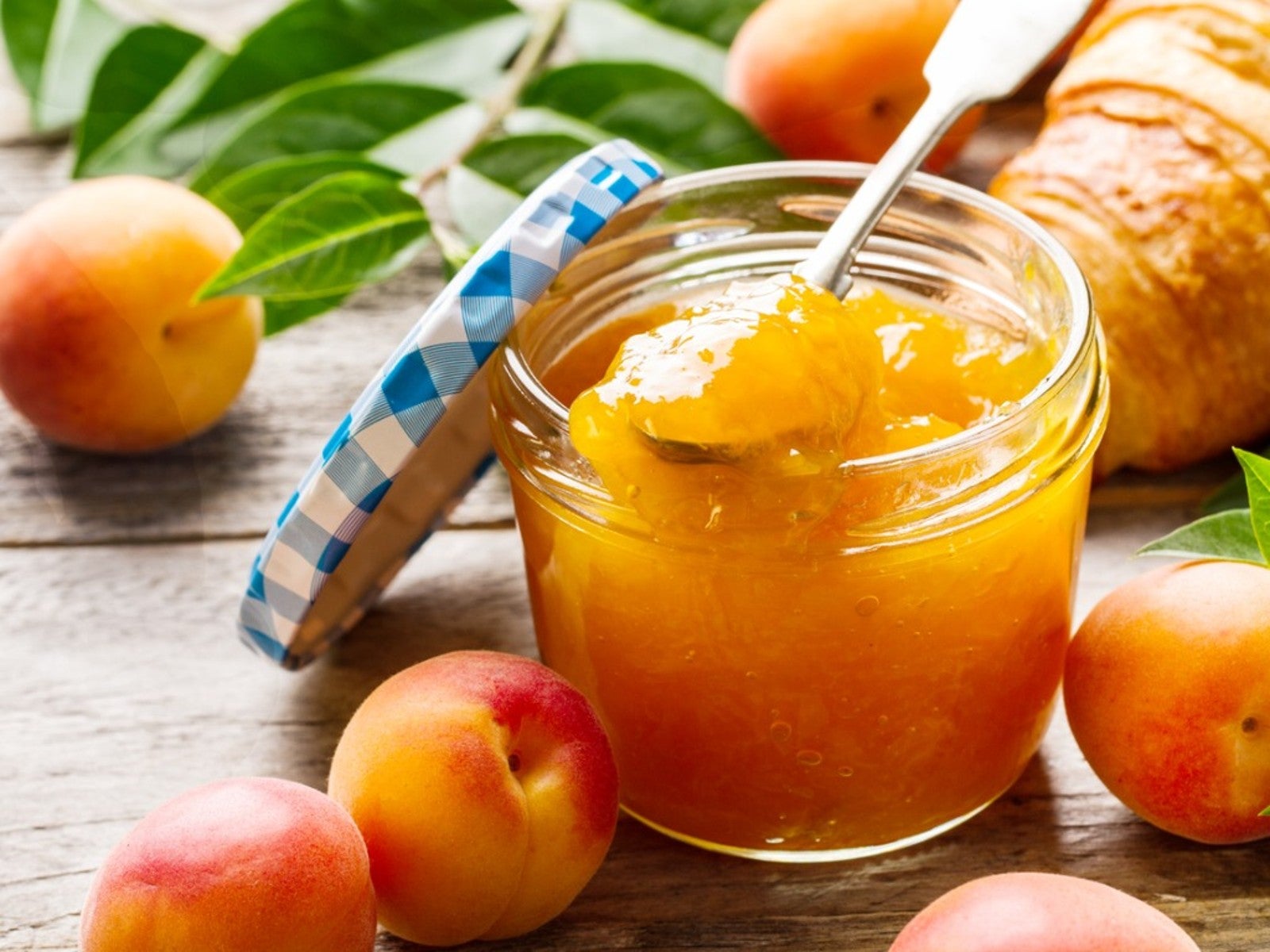 An open jar of apricot preserves surrounded by several whole ripe apricots