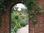 A view through an arched brick doorway leads to a beautiful flowering garden