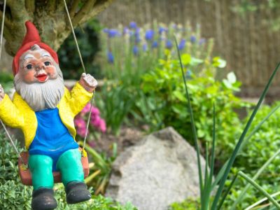 A colorfully dressed garden gnome hanging on a swing in a garden