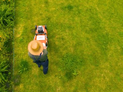 Overhead view of a man in a straw hat mowing a lawn