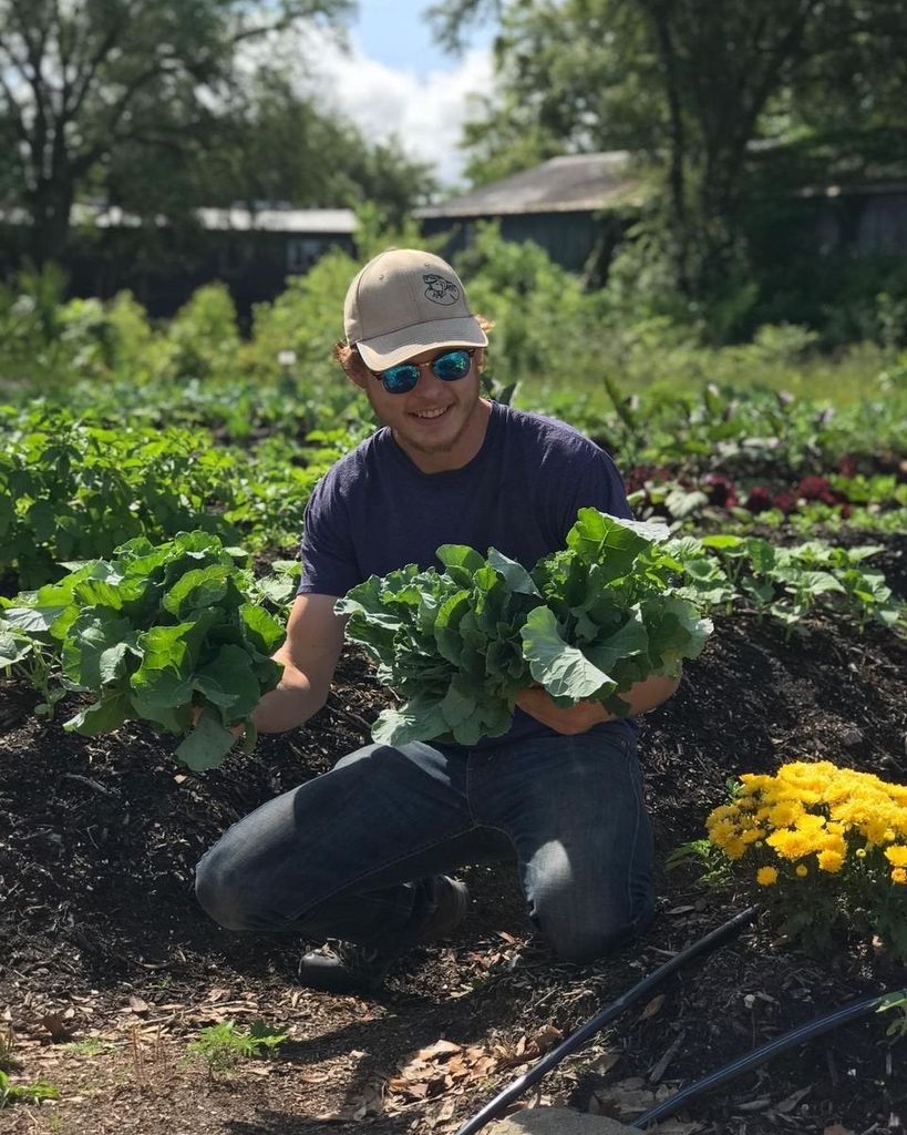 A smiling man holds greens in a garden