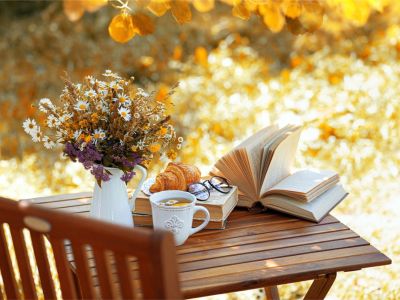 A book, vase of flowers, glasses, and mug on a small table outdoors