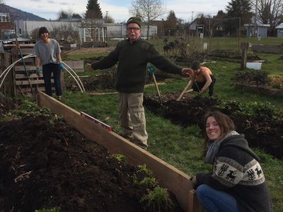 Three smiling people work on a raised garden bed
