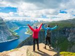 Two hikers stand over a fjord with their arms raised