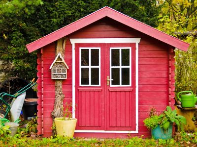 A light red small shed, with some garden tools around it