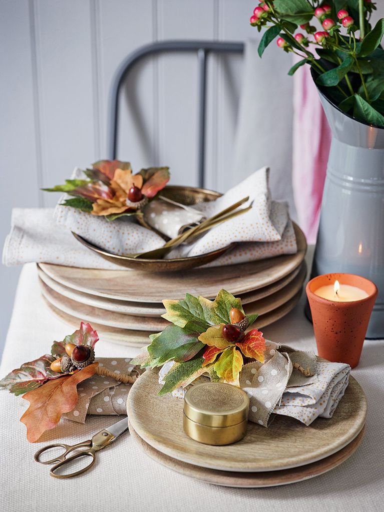 Napkin decorations made from autumn leaves and acorns, laid on top of napkins and wooden plates