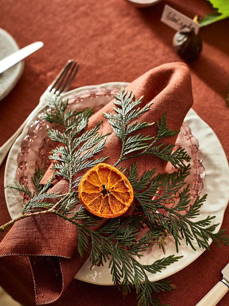 Christmas place setting with a red napkin, foliage and dried orange slice