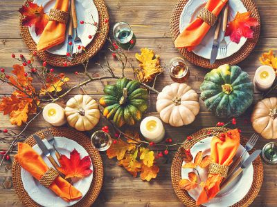 One of the most rustic Thanksgiving table decor ideas featuring gourds, fall branches, berries, leaves, and candles, all set around plates and orange napkins
