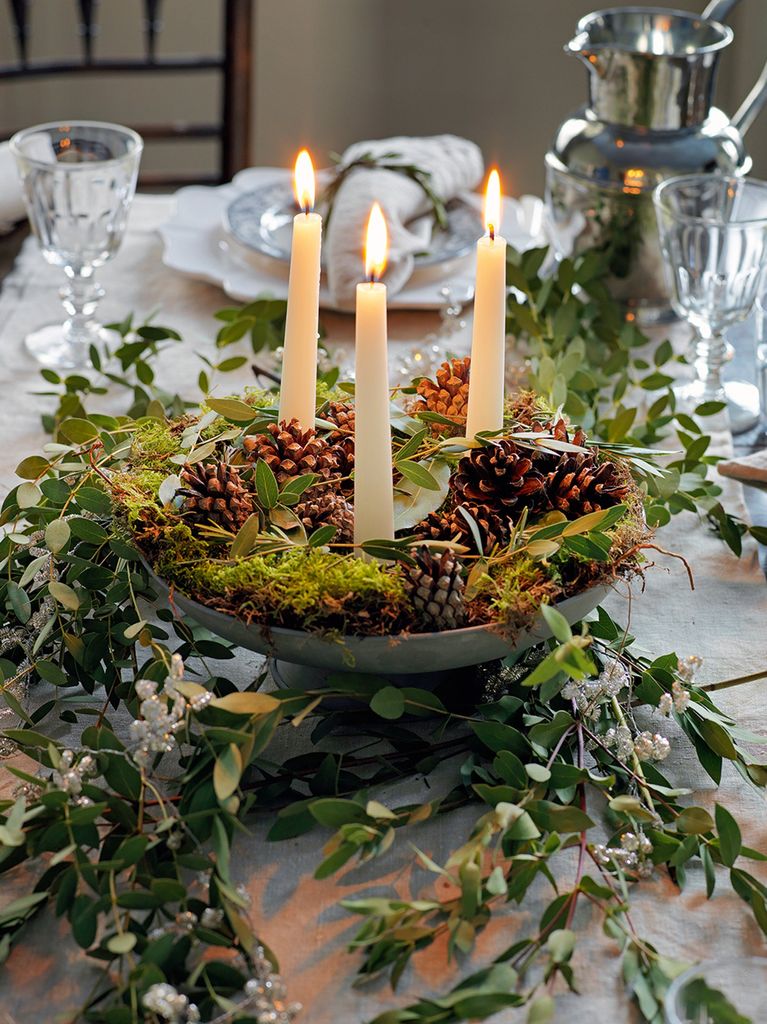Table centerpiece featuringcandles, pine cones, moss, and foliage from the garden
