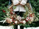 A woman showcasing festive winter wreath ideas, standing in the garden on a patch of snow., holding a foliage and berry wreath.