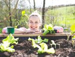 A smiling woman leans on a raised garden bed