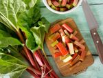 Pieces of rhubarb on a cutting board with a knife and whole rhubarb stalks